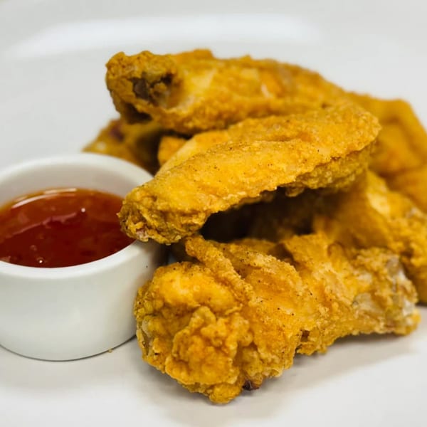 Crispy fried chicken wings with a side of sweet chili dipping sauce on a white plate.