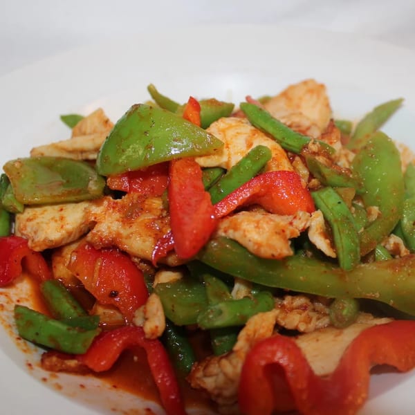 Close-up of a vibrant Thai dish with chicken, red bell peppers, and green beans in a rich sauce.