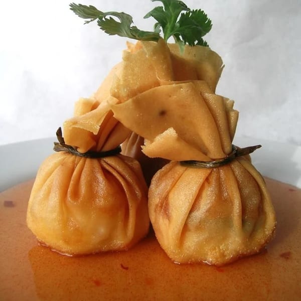 Golden fried Thai money bags, tied with string, sit in a rich orange sauce, garnished with cilantro.