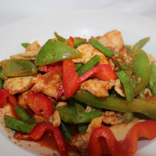 Spicy Thai chicken stir-fry with green beans and red bell peppers on a white plate.