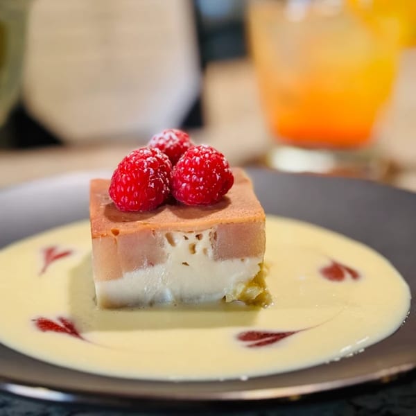Layered dessert with raspberries on top, served with a creamy sauce and red swirls on a dark plate.