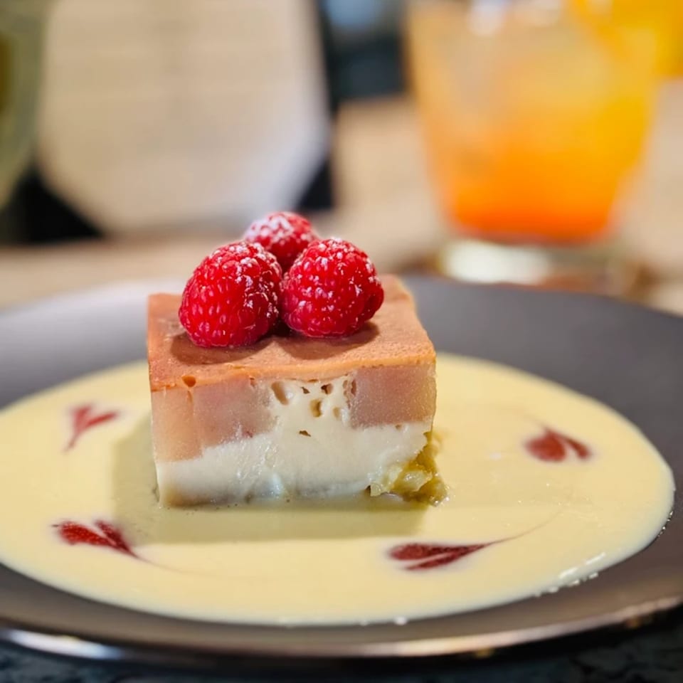 Layered dessert with raspberries on top, served with a creamy sauce and red swirls on a dark plate.