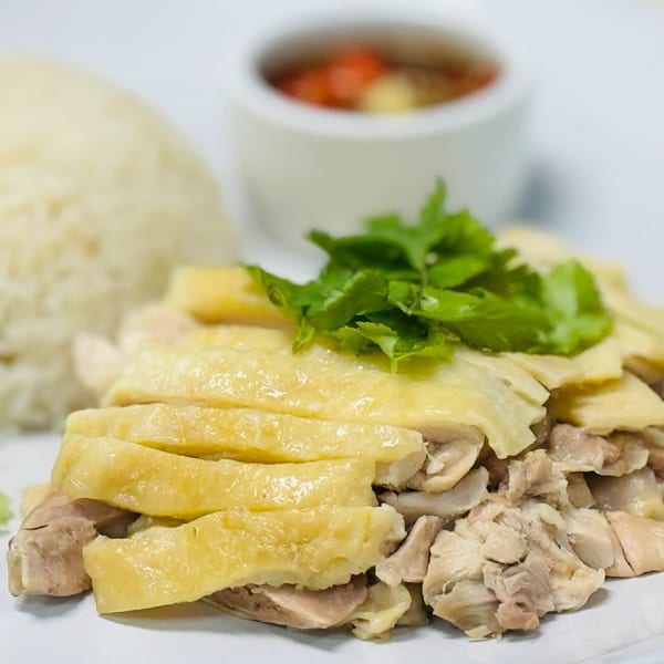 Hainanese chicken rice with sliced chicken, cilantro, and a side of chili sauce at Green Basil Thai Restaurant.
